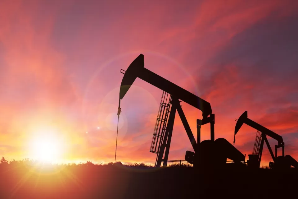Oil well pumpjack sillhouetted against a bright pink sunset sky.